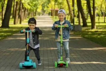 Dos niños montando scooters en un parque.