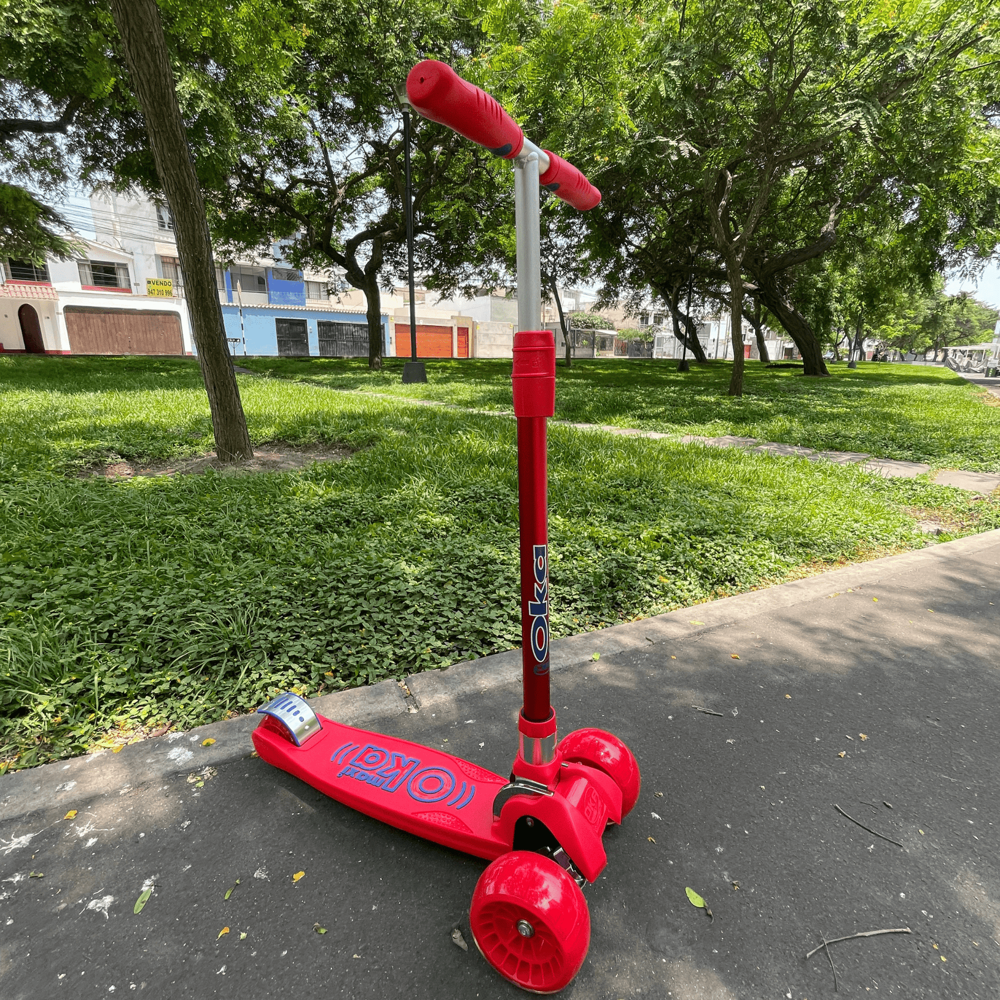 Patinete rojo de tres ruedas marca OKA en un parque.